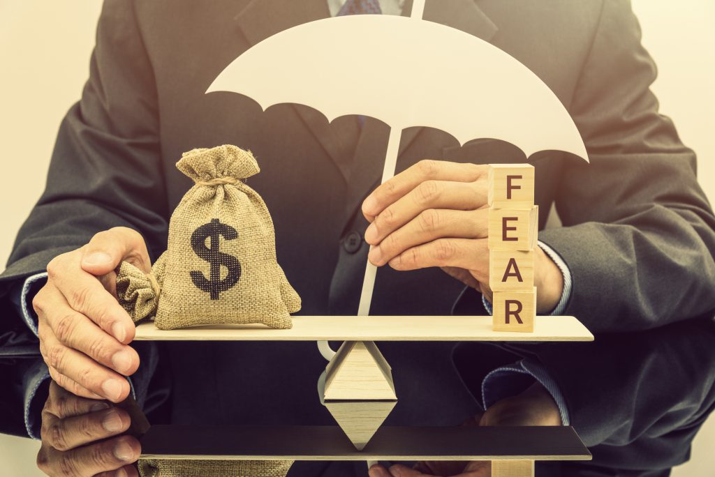 Fear and greed or anxiety in financial market concept : Businessman carries a white umbrella, protects dollar bags or properties on basic balance scale, depicts the influence of emotions on investors