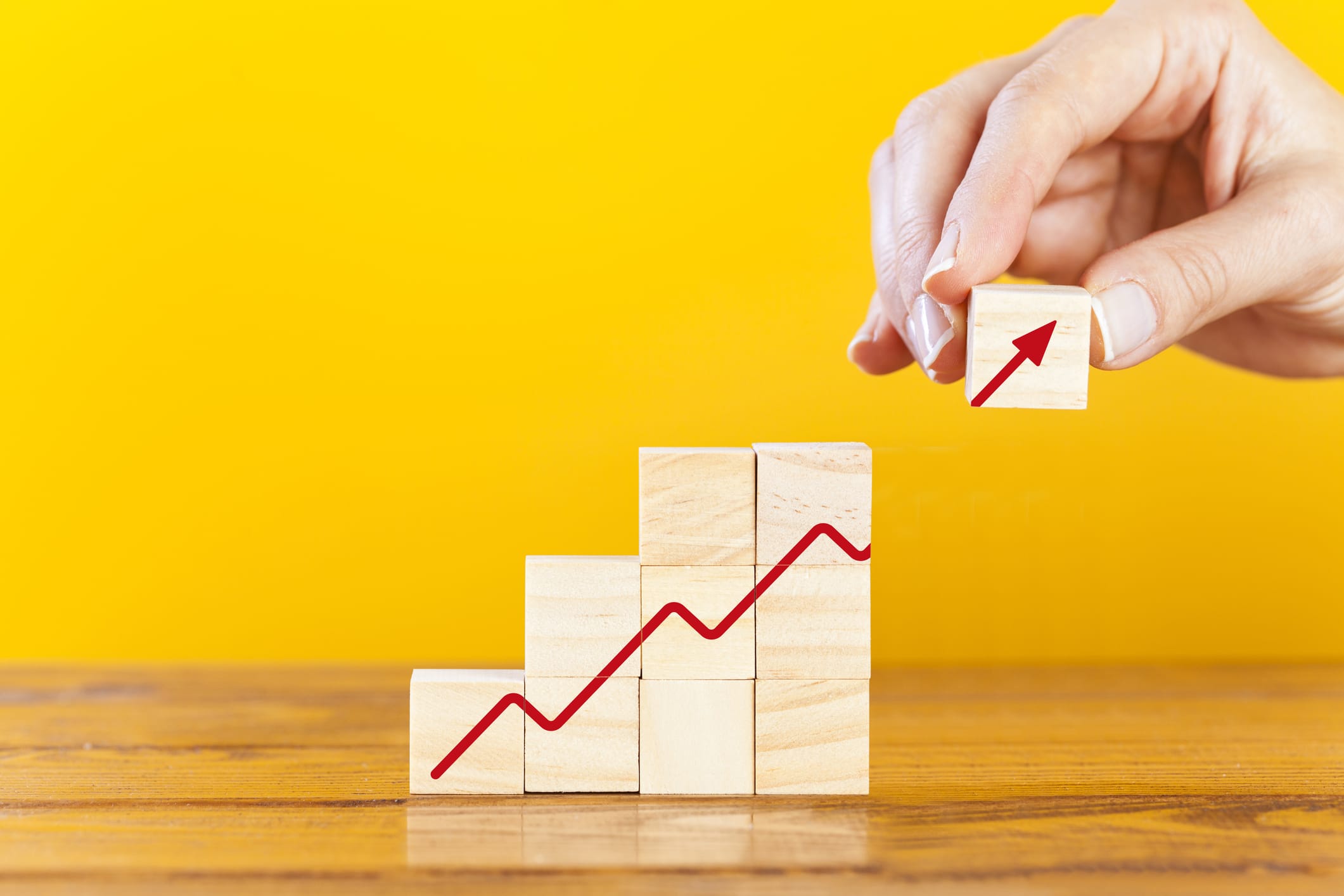 Growing graph on wooden cubes with hand putting last cube with arrow symbol. Financial growth concept