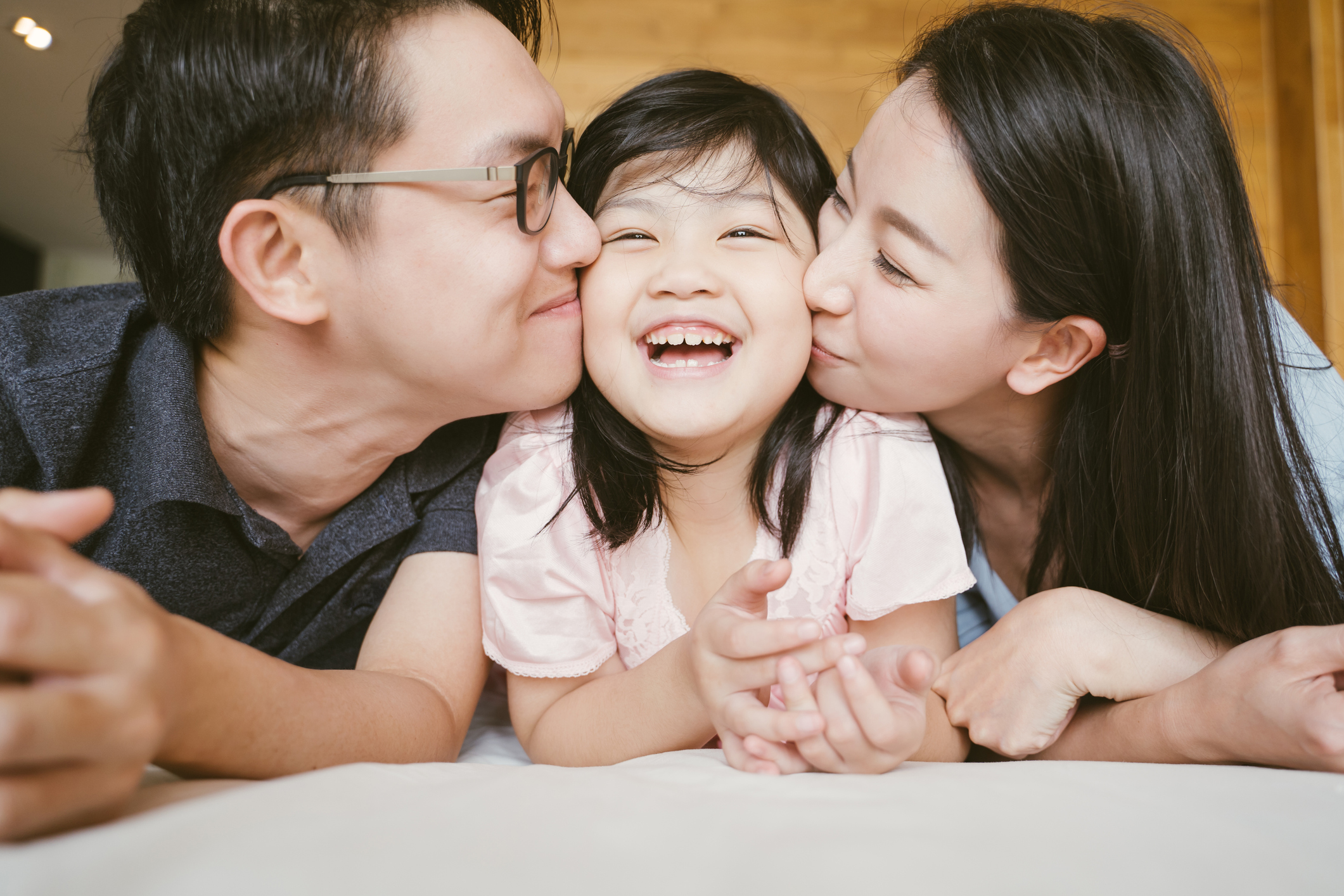 Asian Parents kissing their little daughter on both cheeks. family portrait.