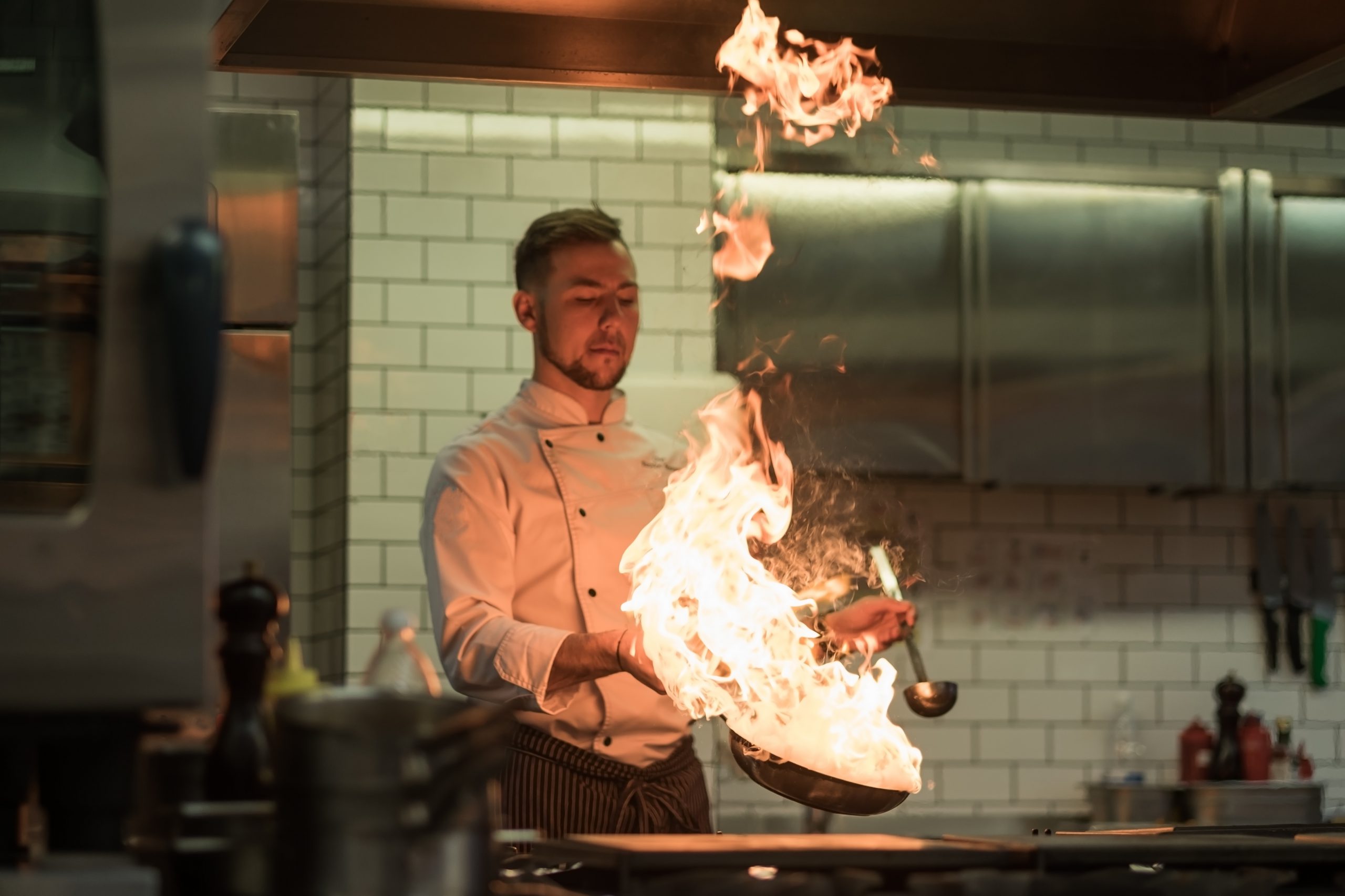 A man cooks cooking deep fryers in a kitchen fire. He gently fry the vegetables while cooking the dish. Focus on fire