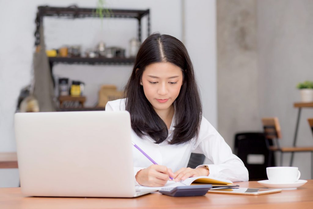 Business asian woman writing on notebook on table with laptop, girl work at coffee shop, freelance business concept.